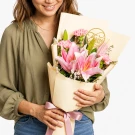 Woman in olive green shirt holding a pink lily and carnation bouquet with a "Thank You" tag.