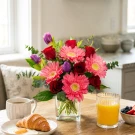 Red roses, pink gerberas, and purple tulips in a clear vase with greenery.