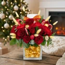Red roses, carnations, candy canes, gold ornaments, and a candle in a square vase with gold ribbon.