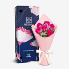 A bouquet of six pink roses in pink paper with a white bow, next to a dark blue box with floral designs.