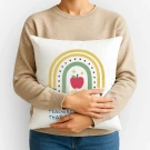 Person holding a pillow with a rainbow and apple design, featuring text about teachers.