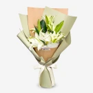 A bouquet of white lilies wrapped in light green and brown paper, tied with a white ribbon.