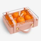 A pink, clear-top trunk filled with six bright oranges, presented as a gift.