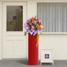 A grand opening flower arrangement of pink gerberas on a red stand, with a white sign.