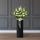 Tall black vase arrangement of white lilies, carnations, roses, and matthiola with a white bow.