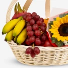 Fruit basket with bananas, grapes, dragonfruit, orange, apple, and sunflower.