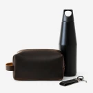Brown leather dopp kit, black insulated tumbler, and black leather keychain on white background.