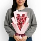 Woman holding a pink-wrapped bouquet of 7 individual KitKat bars, tied with a maroon ribbon.