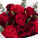 Red roses, carnations, and pom poms with eucalyptus leaves in a bouquet.
