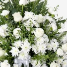 White roses, mums, and carnations arranged in a sympathy stand with greenery and a white ribbon.