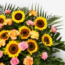 Sunflowers, pink and orange carnations, and green foliage in a celebratory arrangement.