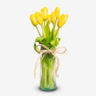 Yellow tulips in a clear glass vase, tied with a twine bow.