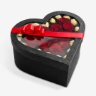 Heart-shaped black box with red roses and gold-wrapped chocolates, tied with a red ribbon.