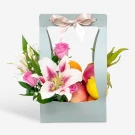 Gift box with lilies, roses, and assorted fruits, tied with a bow.