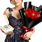 Woman holding a bouquet of red roses and a small cake with "Happy anniversary to us" written on it.