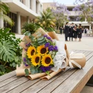 Sunflowers, purple statice, and eucalyptus in brown paper wrapping, tied with a white ribbon.