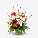 A vibrant bouquet of red anthuriums, white lilies, and pink pussy willows in a glass vase.