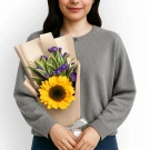 Woman holding a bouquet with a large sunflower, violet statice, and green leaves.