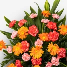 An arrangement of vibrant orange gerberas and pink and red carnations with green foliage.
