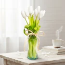 White tulips in a green vase tied with a raffia ribbon, with a blurred background.