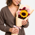 Woman holding a bouquet of sunflowers, pink carnations, and dark red flowers.