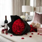 A bouquet of 50 vibrant red roses wrapped in black paper, tied with a red ribbon.