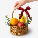 Wicker fruit basket with bananas, oranges, apples, and eucalyptus, adorned with a red ribbon.