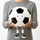 A person holds a plush soccer ball with a smiling face and short legs wearing sneakers.
