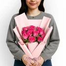 Woman holding bouquet of 12 pink roses in pink paper.