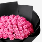 Close-up of a large bouquet of bright pink roses wrapped in black paper.