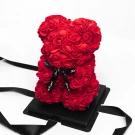 Red rose teddy bear with black ribbon on black base, against white background.