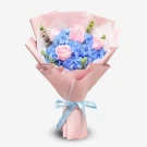 Pink roses and blue hydrangeas in a pink bouquet with a blue ribbon.
