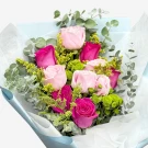 A bouquet of pink roses and green button mums with eucalyptus, wrapped in blue and white paper.