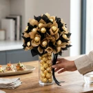 A bouquet of 40 Ferrero Rocher chocolates in gold wrappers, arranged in a glass vase with black and gold paper accents.