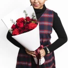 Woman in plaid vest holding a bouquet of red roses and carnations.