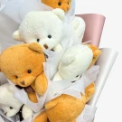 Several fluffy brown and white teddy bears with bows nestled in a white box with pink ribbon.