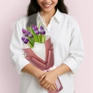 Woman in white shirt holding purple tulips decorated with rhinestones, wrapped in pink paper.