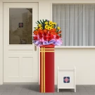 A red flower stand with a vibrant bouquet of orange, red, and yellow gerbera daisies with purple and pink wrapping.