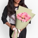 Woman holding a bouquet of pink gerberas and carnations wrapped in light green paper.