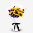 Bouquet of sunflowers and purple statice flowers wrapped in white paper, tied with a black ribbon.