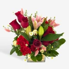 Red roses, lilies, and carnations with gold ornaments in a clear vase.