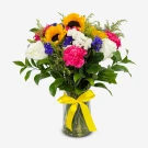 A vibrant bouquet of sunflowers, roses, and carnations in a glass vase, tied with a yellow ribbon.
