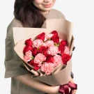 Woman holding a bouquet of red roses and pink carnations wrapped in brown paper.