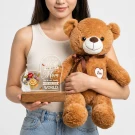 Person holding brown teddy bear and heart-shaped acrylic plaque with flowers and text for mom.