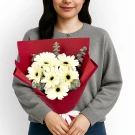 White gerberas and eucalyptus bouquet wrapped in red paper, held by a person in a gray sweater.