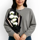 Woman in gray cardigan holding a bouquet of white carnations wrapped in black paper.