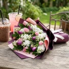 Bouquet of purple and pink tulips with white flowers and green leaves, wrapped in pink and purple paper with a white ribbon.