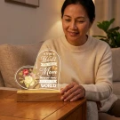 Woman smiling beside a heart-shaped lamp with flowers and "Mom" text.