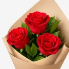 Three red roses with green leaves, wrapped in brown paper.