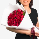 Woman holding a large bouquet of 24 vibrant red roses wrapped in white paper.